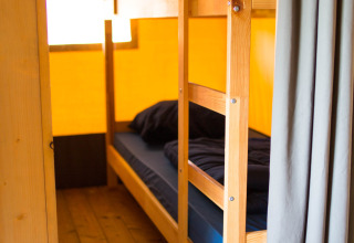 Litera con ropa de cama oscura en una tienda safari con suelo de madera en Camping de Boomgaard, Bélgica.