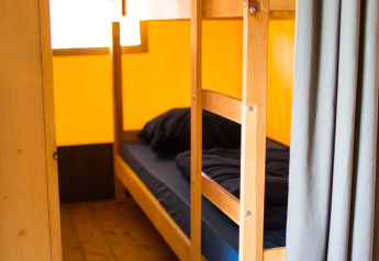 Litera con ropa de cama oscura en una tienda safari con suelo de madera en Camping de Boomgaard, Bélgica.