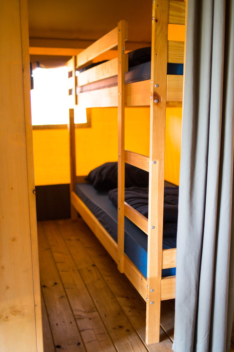 Køjeseng med mørkt sengetøj i en safari-telt med trægulv på Camping de Boomgaard i Belgien.