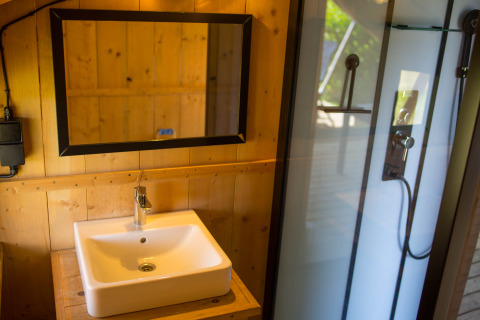 Bagno moderno con pareti in legno, lavabo, specchio e doccia in una tenda safari in Belgio.