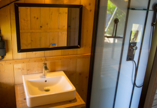 Baño moderno con paredes de madera, lavabo, espejo y ducha en una tienda safari en un camping en Bélgica.