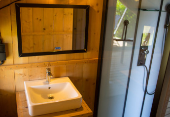 Bagno moderno con pareti in legno, lavabo, specchio e doccia in una tenda safari in Belgio.