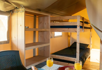 Interior of a safari tent with bunk beds, set dining table with bread rolls and orange juice for breakfast.