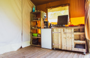 Cucina rustica in legno con fornello, frigorifero e scaffali in una tenda safari al Camping de Boomgaard.