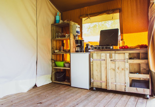 Cozy wooden kitchen setup with stove, fridge and shelves inside a safari tent at Camping de Boomgaard, Belgium.