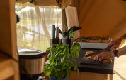 Cucina accogliente in tenda safari al Camping de Boomgaard, Belgio, con una persona che taglia il pane.