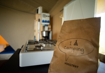 Interno di tenda safari con fornello a gas e sacchetto di carta ‘I love camping’ di Vodatent.