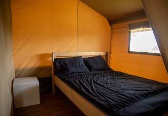 Innenansicht eines Safari-Zeltes mit einem einfachen Holzbett, schwarzer Bettwäsche und kleinem Tisch.