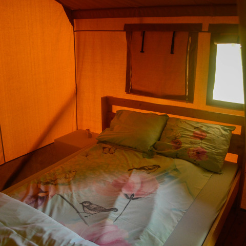 Vista interna di una tenda safari con letto matrimoniale e finestre, Safari tent al Camping du Rivage in Lussemburgo.