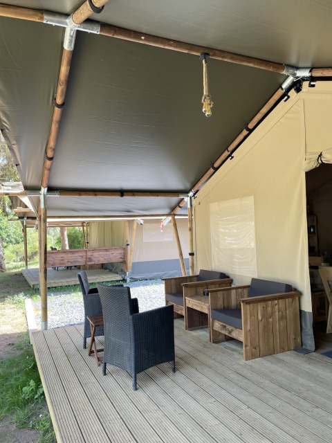 Safari tent met houten terras en zithoek bij Camping du Rivage in Luxemburg, omgeven door natuur.