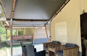 Safari tent with wooden deck and seating area at Camping du Rivage in Luxembourg, surrounded by nature.