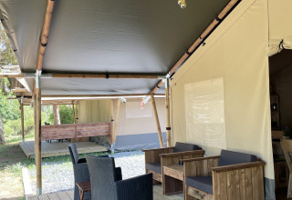 Tienda safari con terraza de madera y asientos en Camping du Rivage en Luxemburgo, rodeada de naturaleza.