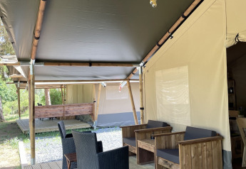 Safari tent with wooden deck and seating area at Camping du Rivage in Luxembourg, surrounded by nature.