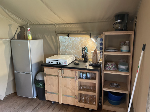 Keukengedeelte in de safaritent bij Camping du Rivage in Luxemburg, met koelkast, rekken en kookplaat.