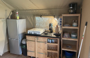 Coin cuisine dans la tente safari au Camping du Rivage au Luxembourg avec réfrigérateur, étagères et cuisinière.