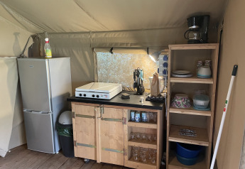 Køkkenområde i safaritelten på Camping du Rivage i Luxembourg med køleskab, hylder og komfur.