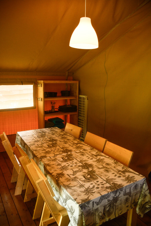 Interieur van een safaritent op Camping du Rivage in Luxemburg met tafel, stoelen en rek.