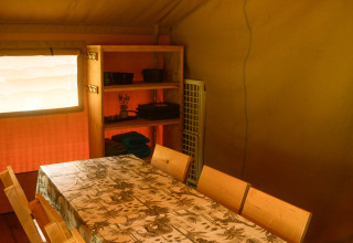 Interior de una tienda safari en Camping du Rivage, Luxemburgo, con mesa comedor, sillas y estantería.