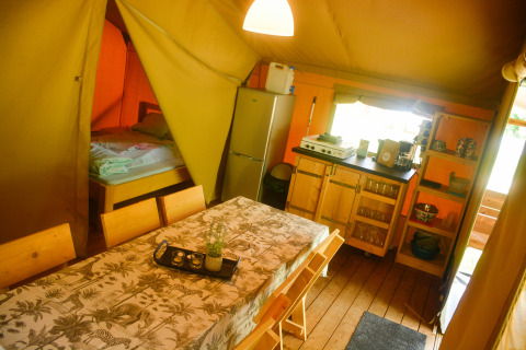 Binnenkant van safaritent bij Camping du Rivage in Luxemburg met eettafel, keuken en bedhoek.