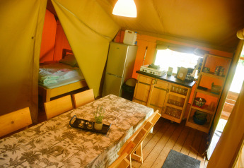 Interno della tenda Safari al Camping du Rivage in Lussemburgo con tavolo da pranzo, cucina e letto.
