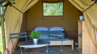 Safari-Zelt Duo Lodge auf Camping de Boomgaard in Belgien mit Bett, Tisch und Stühlen auf der Terrasse.