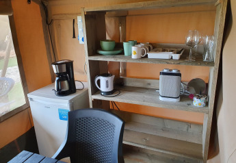 Rincón de cocina en tienda safari con estantes de madera, vajilla, cafetera y mini nevera.