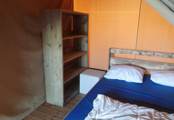 Interior de una tienda safari en Camping de Oude Rijn, Países Bajos, con cama y estantería de madera.