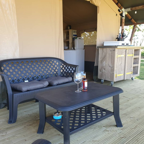 Zona de estar exterior en una tienda safari en Camping Eefting, Países Bajos, con sofá, mesa y cocina.