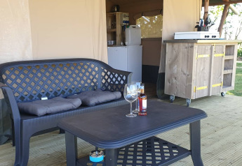 Zona lounge esterna con divano, tavolo e cucina in una tenda safari a Camping Eefting nei Paesi Bassi.