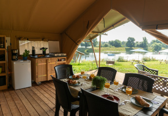 Interno di tenda safari con tavolo da pranzo, cucina e vista fiume al Camping de Boomgaard in Belgio.