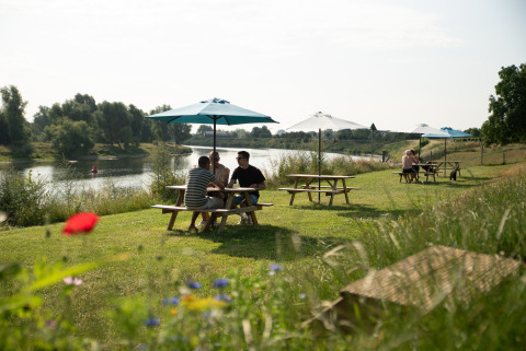 Folk nyder at sidde ved borde med parasoller ved en flod ved Safari tent premium Maaszicht i Belgien.