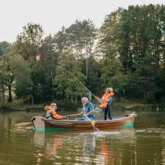 Famiglia che pesca insieme su una barca a remi in un lago in un villaggio vacanze con glamping nel verde.