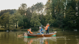 Familia pescando juntos en un bote en un lago, en un parque vacacional con glamping y árboles verdes.