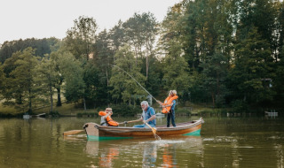 Familia pescando juntos en un bote en un lago, en un parque vacacional con glamping y árboles verdes.