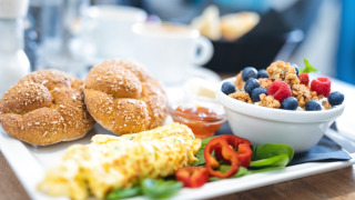 Plato de desayuno con tortilla, panecillos, muesli con bayas y verduras frescas, servido en la mesa.