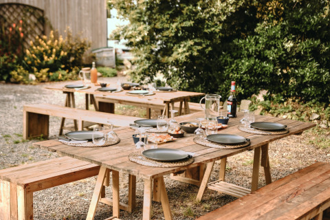 Udendørs picnicområde med træborde og bænke dækket op ved Feather Down Les Jardins des Coccinelles i Bretagne.