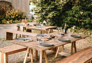 Udendørs picnicområde med træborde og bænke dækket op ved Feather Down Les Jardins des Coccinelles i Bretagne.