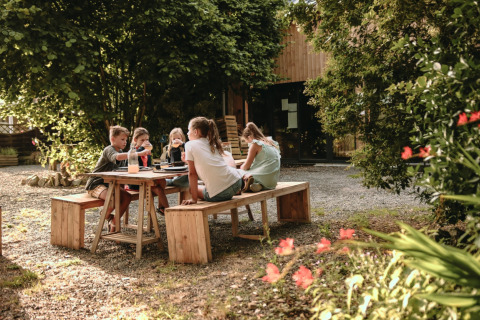 Niños sentados juntos en una mesa de madera al aire libre en Feather Down Les Jardins des Coccinelles, Bretaña, Francia.