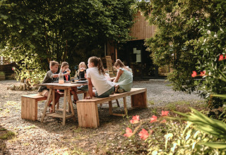 Bambini seduti a un tavolo di legno all'aperto a Feather Down Les Jardins des Coccinelles, Bretagna, Francia.