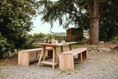 Udendørs picnicbord med bænke og morgenmad ved Feather Down Les Jardins des Coccinelles i Bretagne, Frankrig.