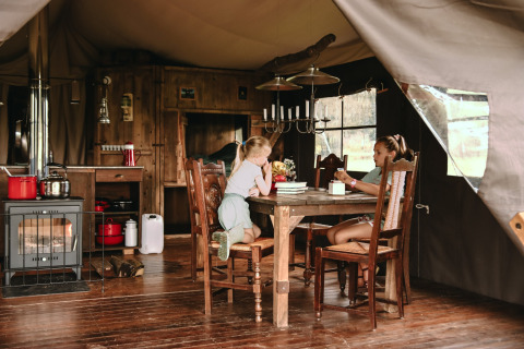 Twee kinderen zitten aan een houten tafel in een tent met houtkachel op een vakantiepark in Bretagne, Frankrijk.