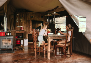 Due bambini seduti a un tavolo di legno in una tenda rustica con stufa a legna in Bretagna, Francia.