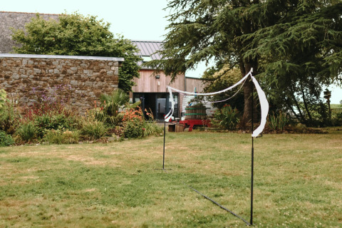 Ein Badmintonnetz steht im Garten neben einem Steingebäude im Ferienpark in der Bretagne, Frankreich.