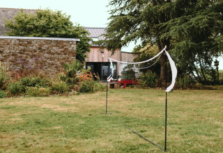 Udendørs badmintonnet sat op i en grøn have ved en stenmursbygning i ferieparken i Bretagne, Frankrig.
