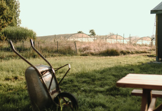 Rural view at Feather Down Les Jardins des Coccinelles, Brittany, with a wheelbarrow and greenhouses in the background.