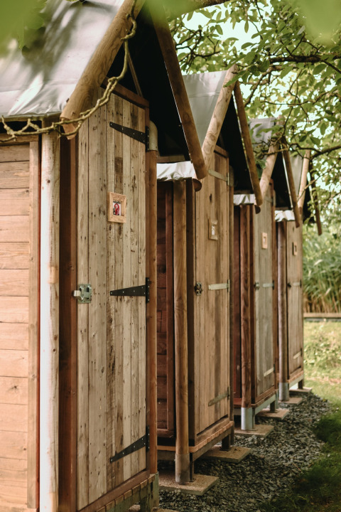 Reihe rustikaler Holztüren von Außentoiletten im Feather Down Les Jardins des Coccinelles, Bretagne, Frankreich.