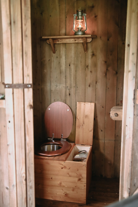 Rustic bathroom with a wooden compost toilet and lantern on a shelf, photographed in Brittany, France.