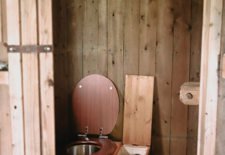 Rustic bathroom with a wooden compost toilet and lantern on a shelf, photographed in Brittany, France.