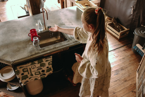 Girl washing hands at a rustic kitchen sink in Feather Down Les Jardins des Coccinelles holiday park, Brittany.