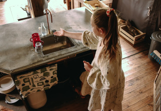 Girl washing hands at a rustic kitchen sink in Feather Down Les Jardins des Coccinelles holiday park, Brittany.